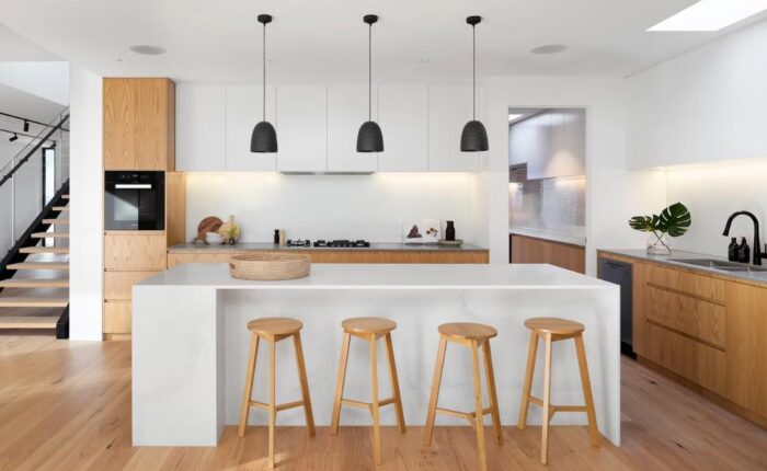 Modern white kitchen with wooden flooring, and 4 stools.